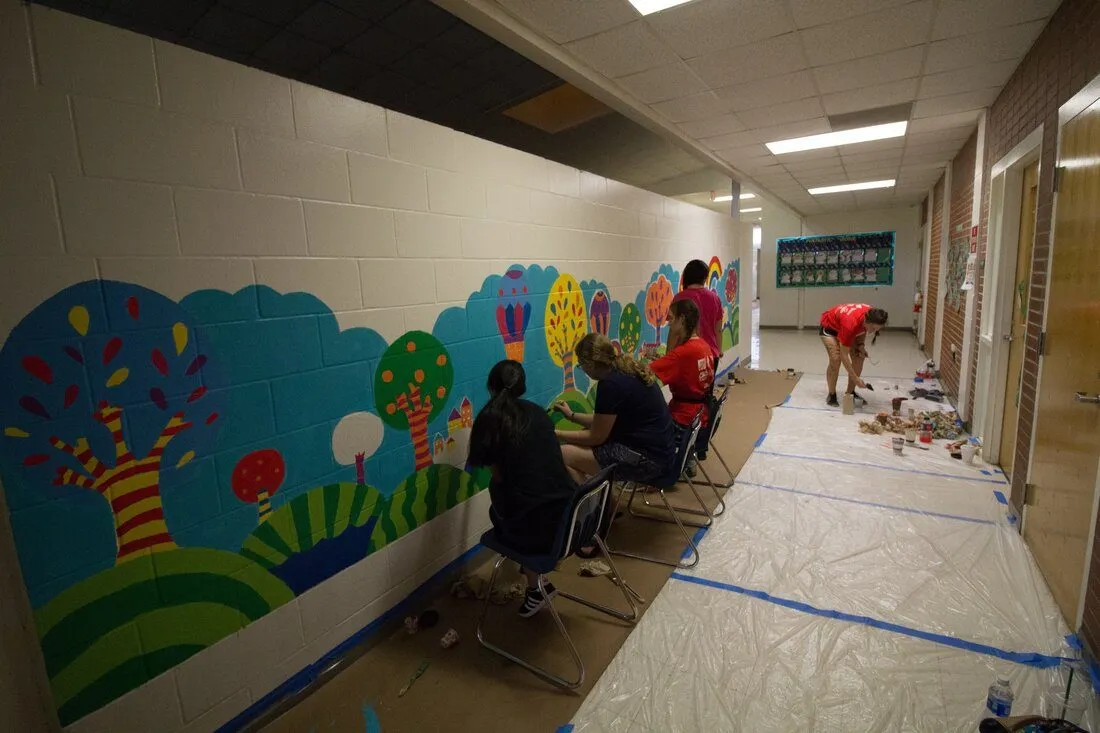 The finished storybook forest mural, volunteers seated adding the last details