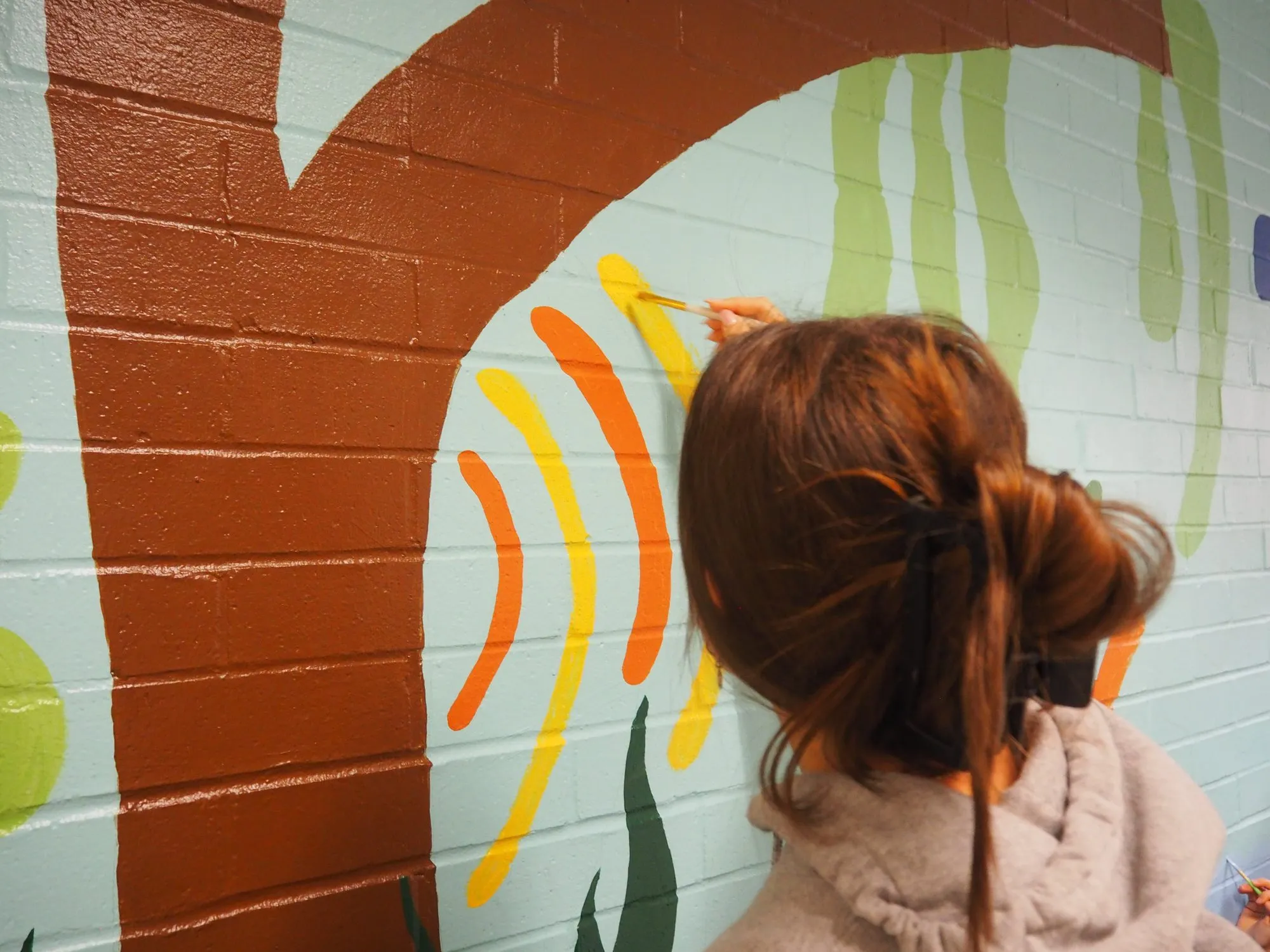 A volunteer painting close details on a tree mural