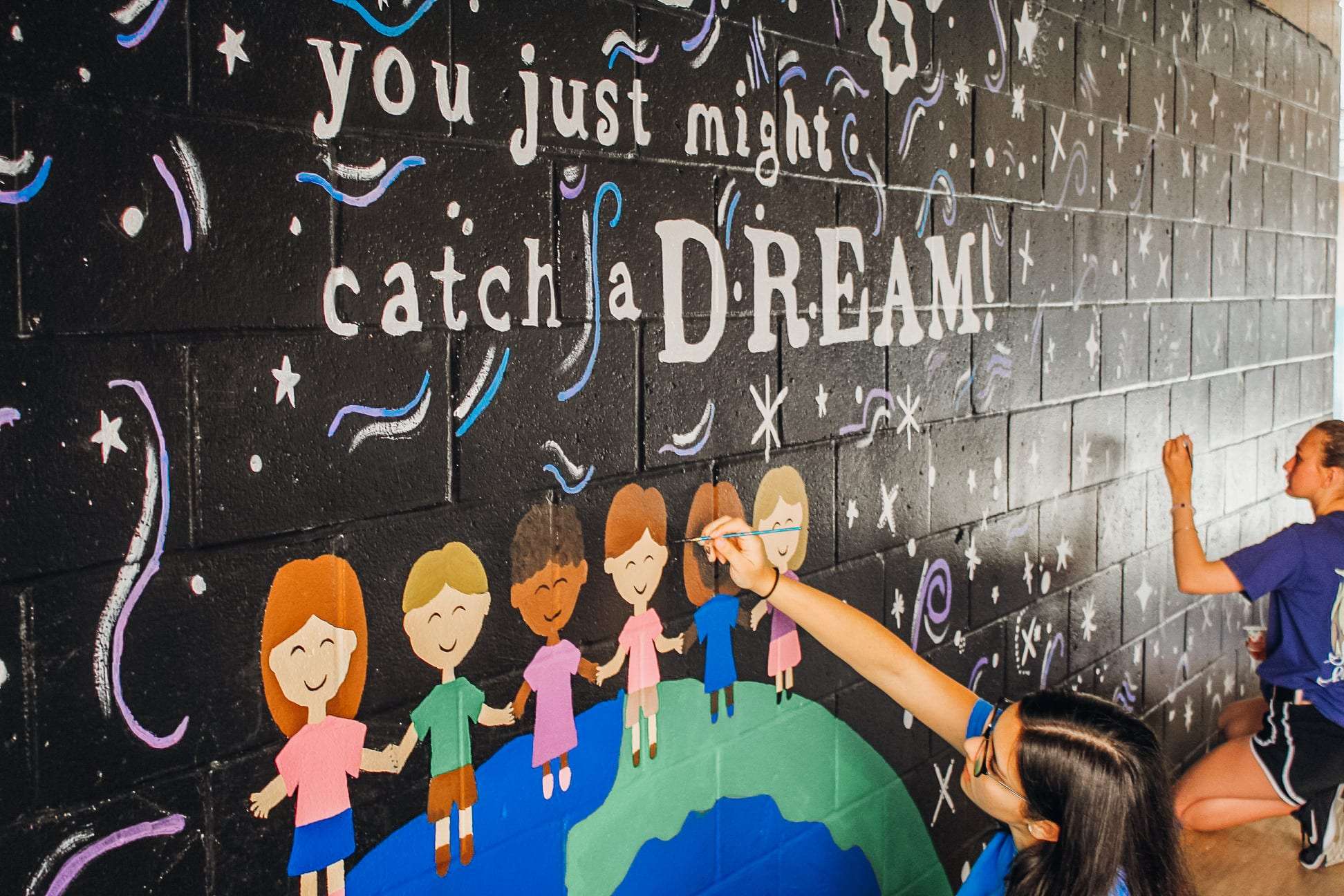 Volunteers painting children around a globe beneath the words You just might catch a dream