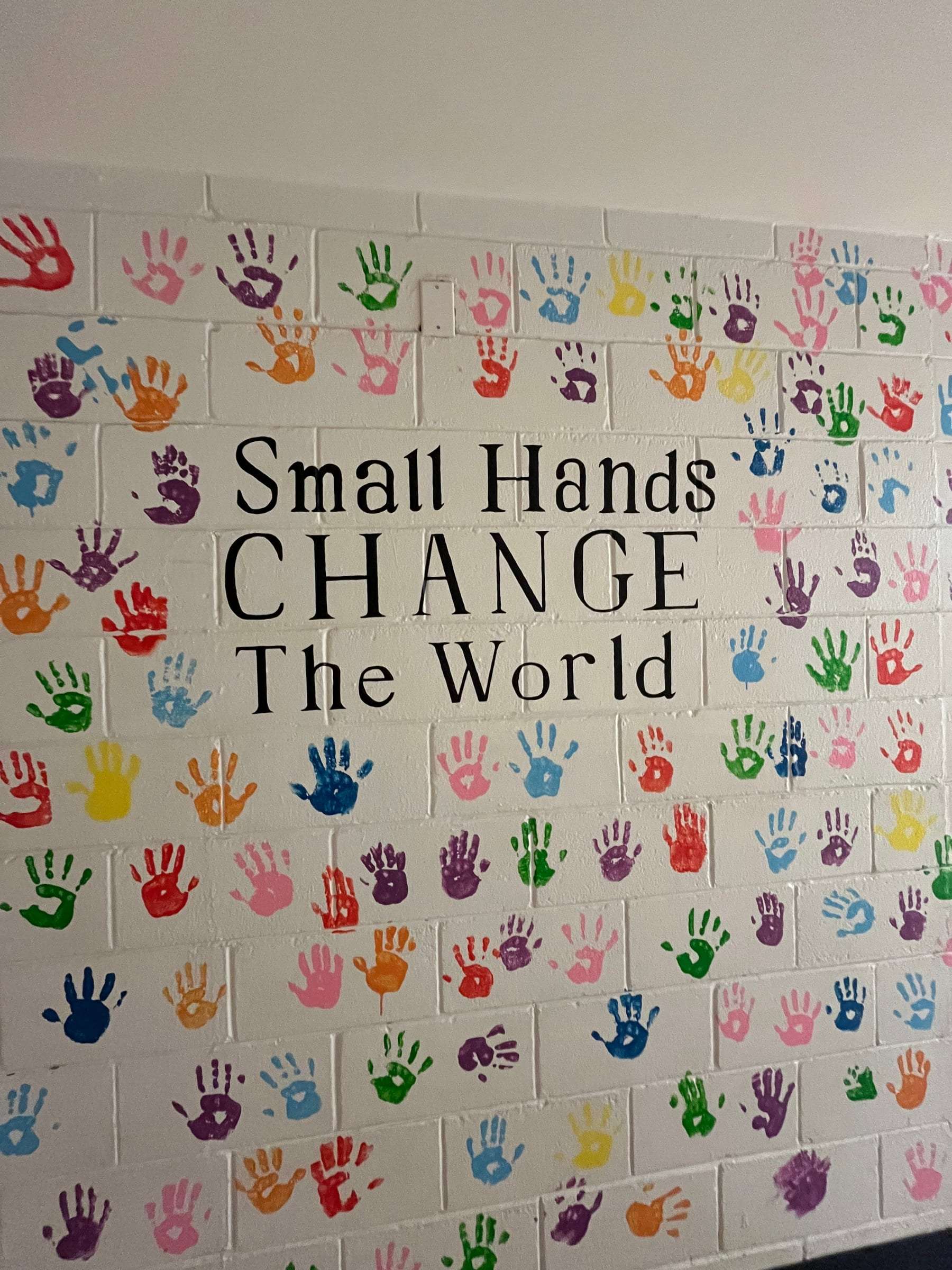 Colorful handprints surrounding the words Small Hands Change The World on a school wall