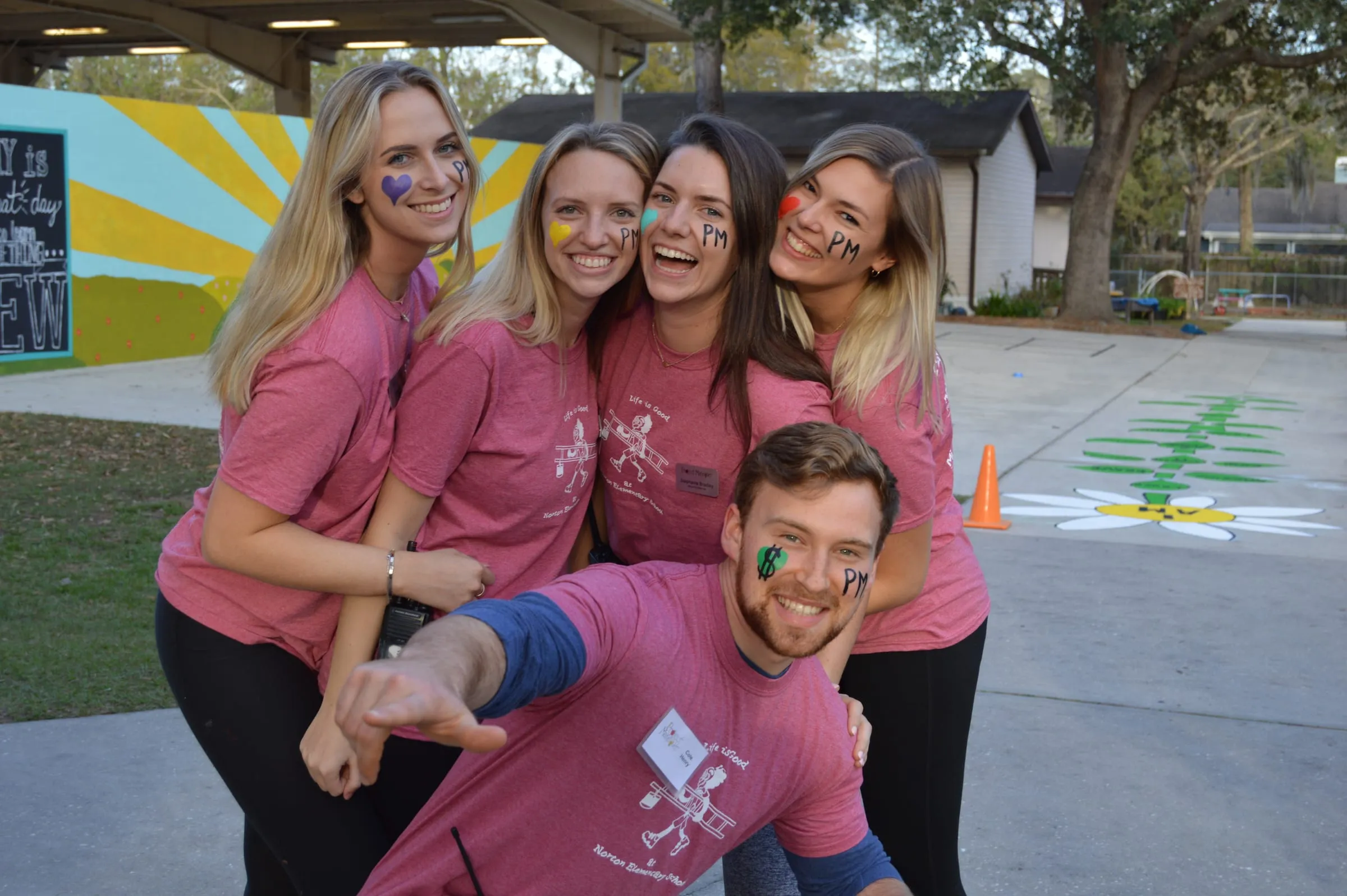 A group of volunteers celebrating together with painted faces after a makeover weekend